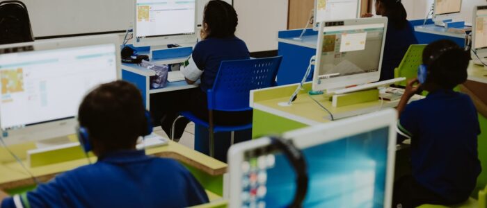 Children engaged in learning at computers in a modern classroom setting, promoting digital literacy.