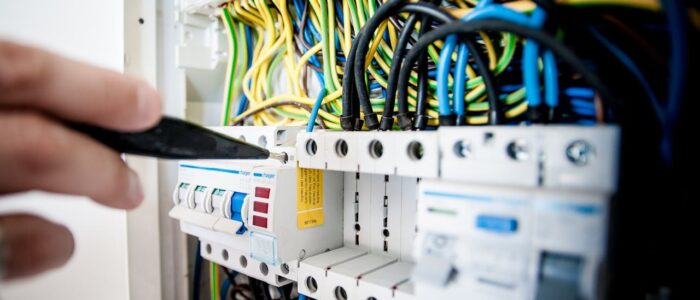 Hand of electrician working on a circuit breaker panel with colorful wires, ensuring safe electrical connections.
