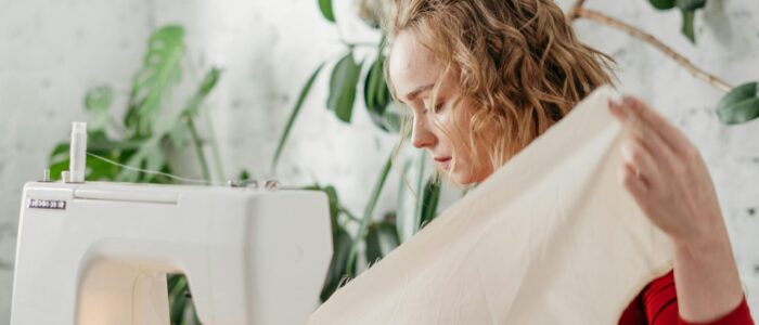 Woman in red dress sewing with a machine in a bright room surrounded by plants.