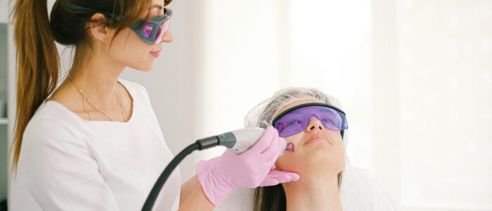 A cosmetologist performing laser treatment on a woman in a clinic setting.